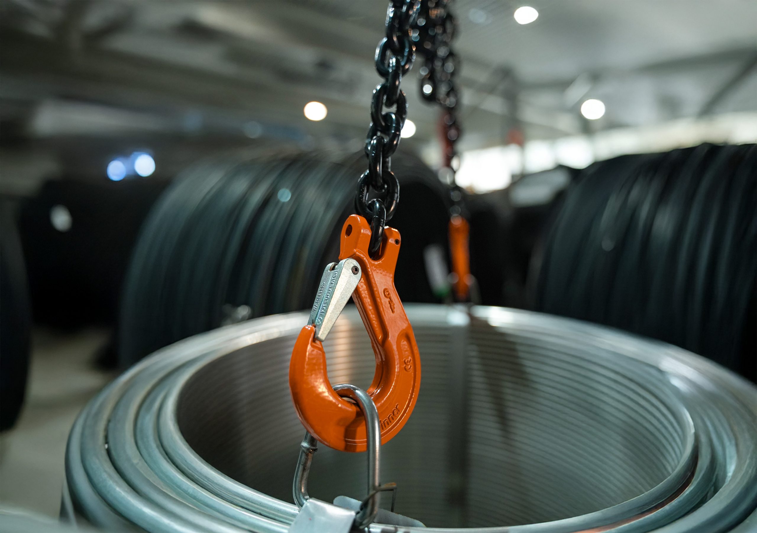 A clevis style lifting hook from pewag lifting a spool of steel cable in an industrial setting