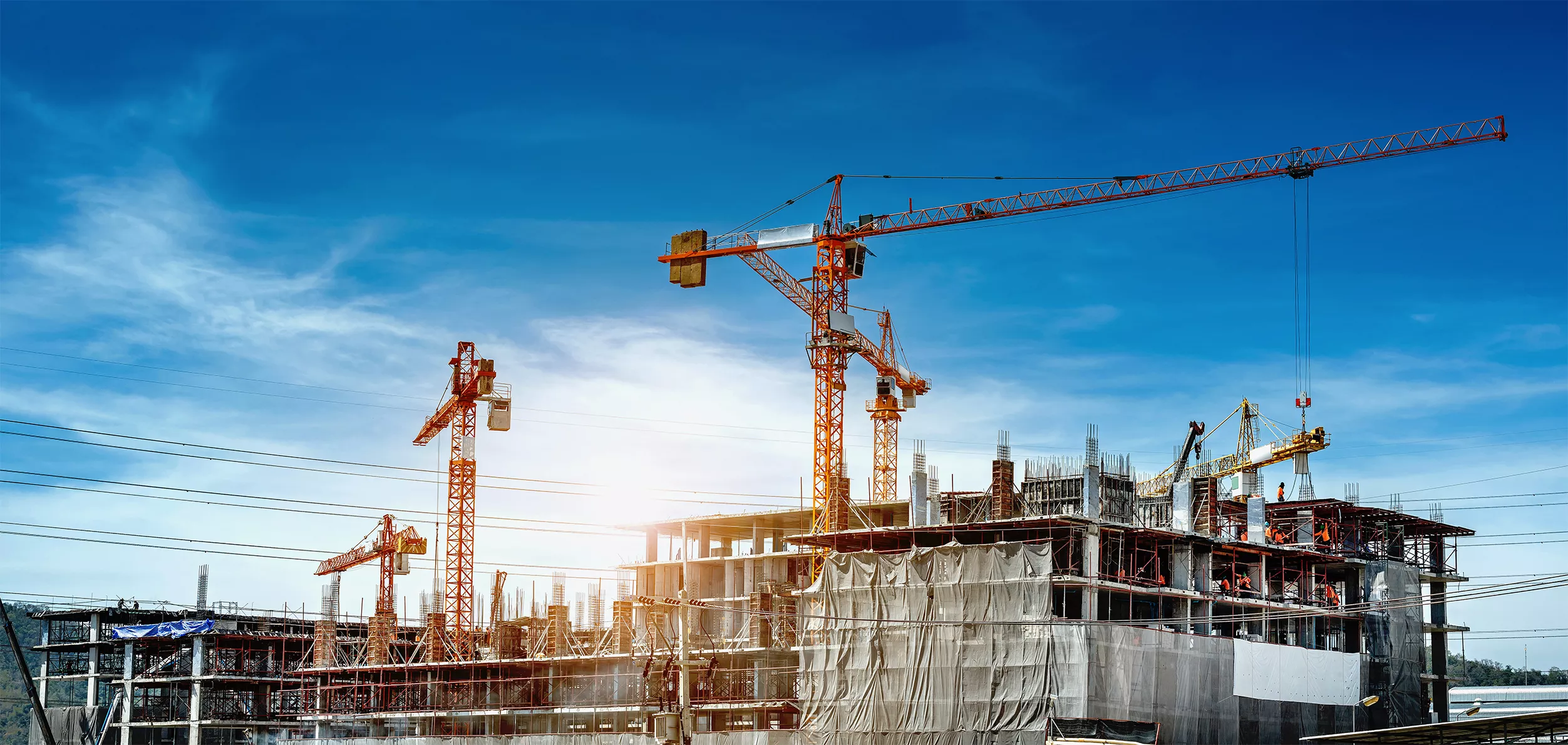 A large building under construction featuring five large cranes with pewag chains and lifting equipment in use