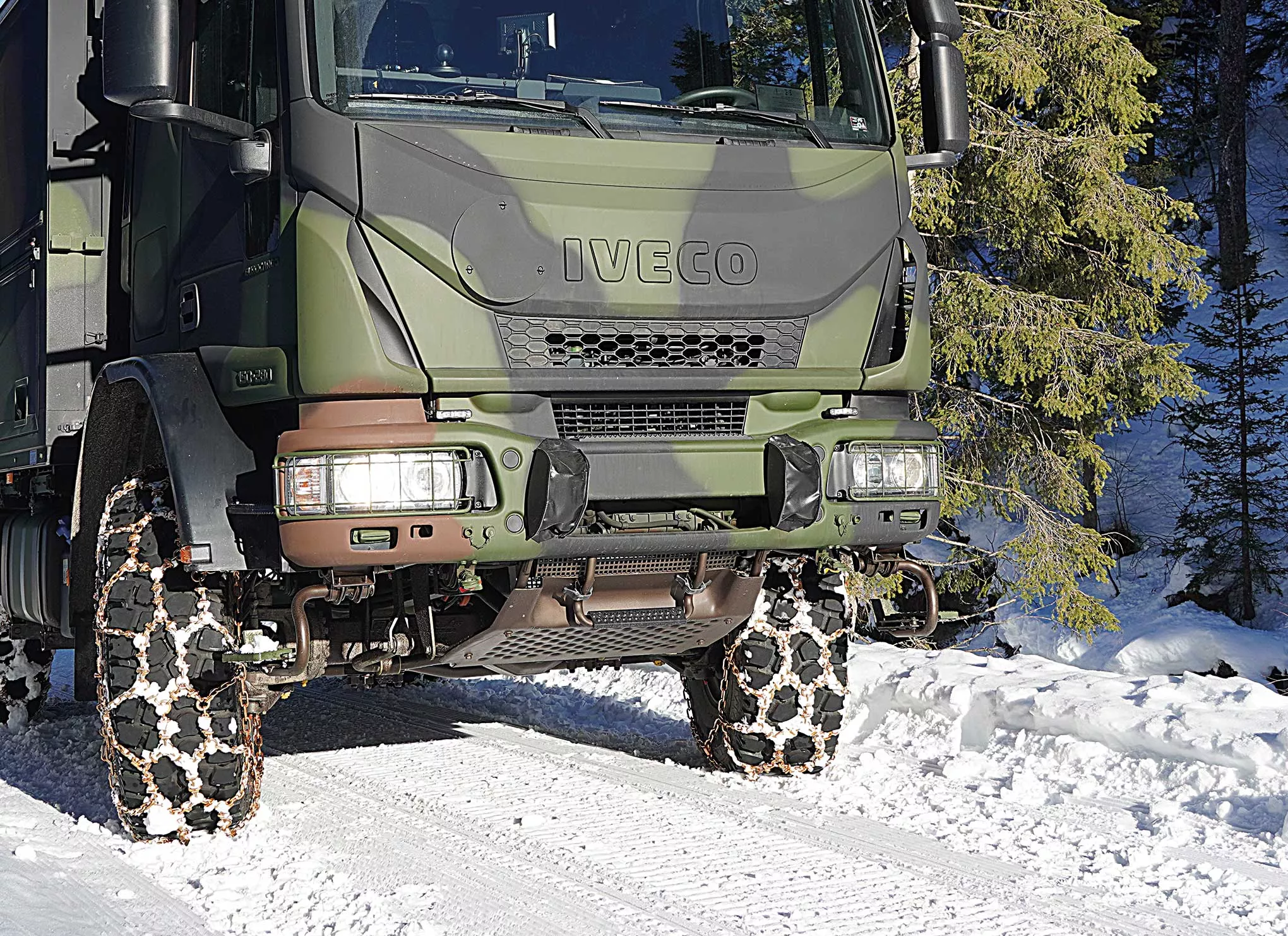 Military truck fitted with traction chains driving through snow