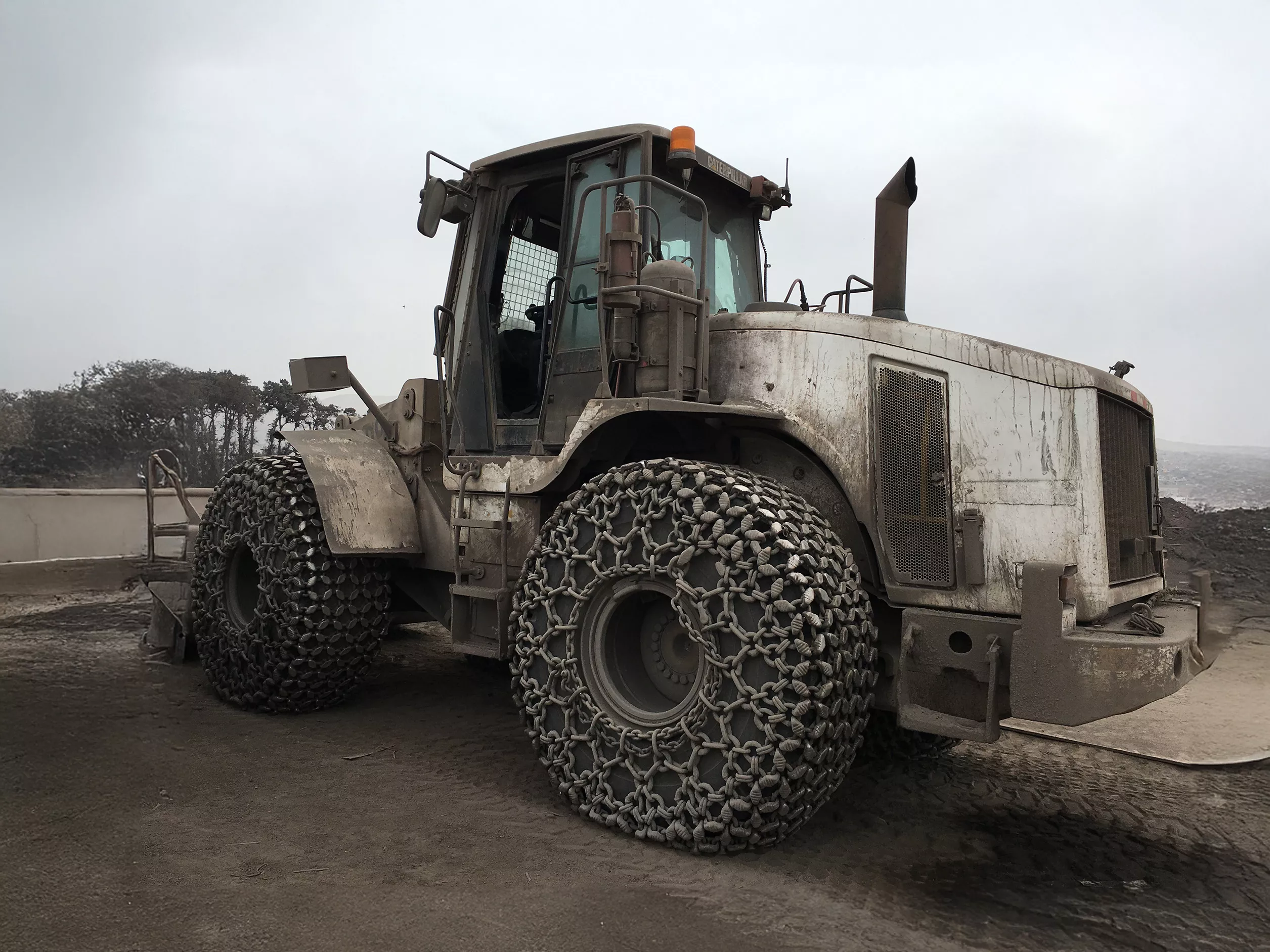 A dirty white construction vehicle in a quarry setting with pewag tire protection chains fitted to all tires.