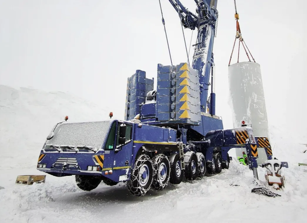 A mobile crane performs a lifting operation in a snowy landscape